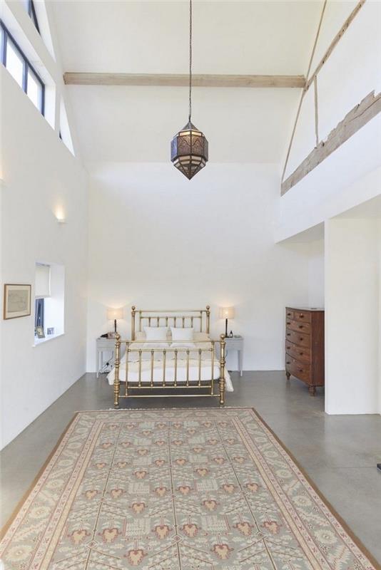 Yaldızlı yatak ve koyu ahşap mobilyalar ile beton zemin üzerinde beyaz yatak odası, yatak odasında ahır düzeni