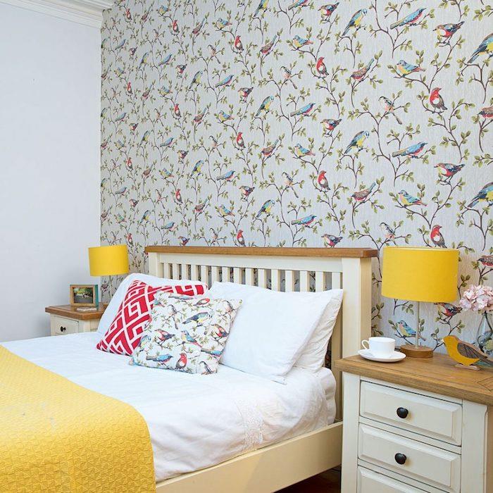 Chinoiserie motifli duvar halısı, ağaç dalları ve renkli kuşlar, ahşap yatak, sarı battaniye ve ahşap komodin ile yetişkin yatak odası dekoru