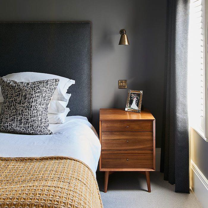 siva barva za spalnico za odrasle, nočna omara z lesenimi predali, ogljeno siva vzglavja, belo perilo in rumena odeja
