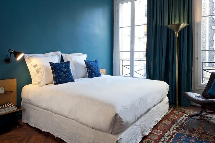 ideja za dekoracijo spalnice za odrasle, temno modra naglasna stena, pavova modra zavesa, belo posteljnina z modrimi okrasnimi blazinami, orientalska preproga, rjavi parket