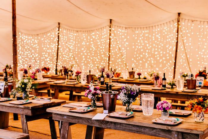 podeželska elegantna poroka, lesene mize in klopi, stekleni kozarci s cvetjem, okras lahkih venčkov, poročni šotor