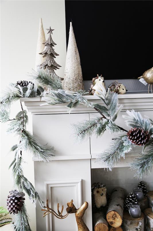 nuotrauka padirbtas dekoratyvinis židinys su baltu kaminu su kalėdiniu papuošimu su dirbtinės eglės girliandos pušies kūgiais iš medinių rąstų židinyje
