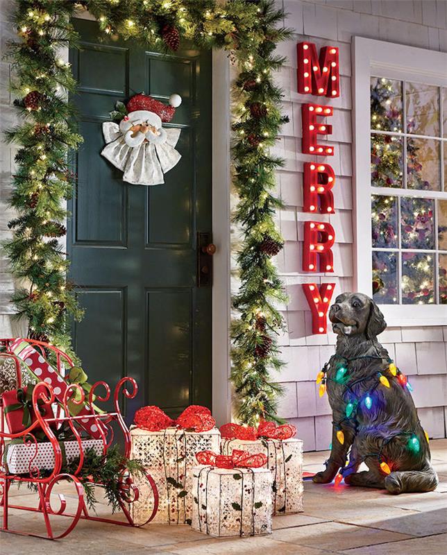 šviesi lauko Kalėdų puošmena su dekoratyviniu šunimi, šalia esančiomis rogėmis ir dovanų dėžutėmis