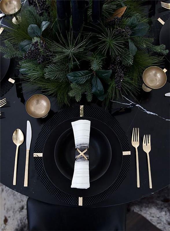 novoletna dekoracija na črni mizi s črnimi krožniki in zlatim priborom