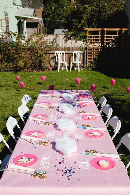 okrasne ideje za rojstnodnevno zabavo na prostem, lepa dekoracija mize z osebno rožnatim prtom z imeni gostov in dodatkom za samorog v bližini vsakega krožnika
