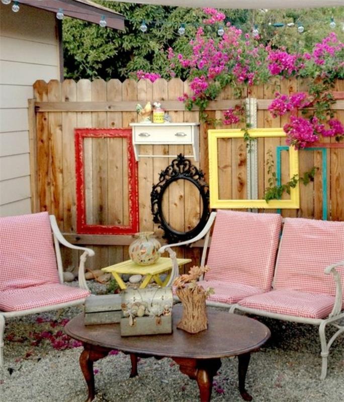 lesena ograja, okrašena s starinskimi praznimi okvirji ovalne in pravokotne oblike ter različnimi barvami, rožami, belimi kovinskimi stoli in blazinami v beli in rdeči barvi, zunanja deko dekoracija