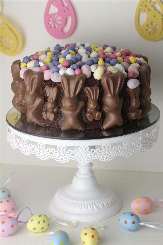 enostavna čokoladna velikonočna torta, okrašena z mini velikonočnimi jajci in večplastnimi čokoladnimi zajčki, ki se sprehajajo okoli torte
