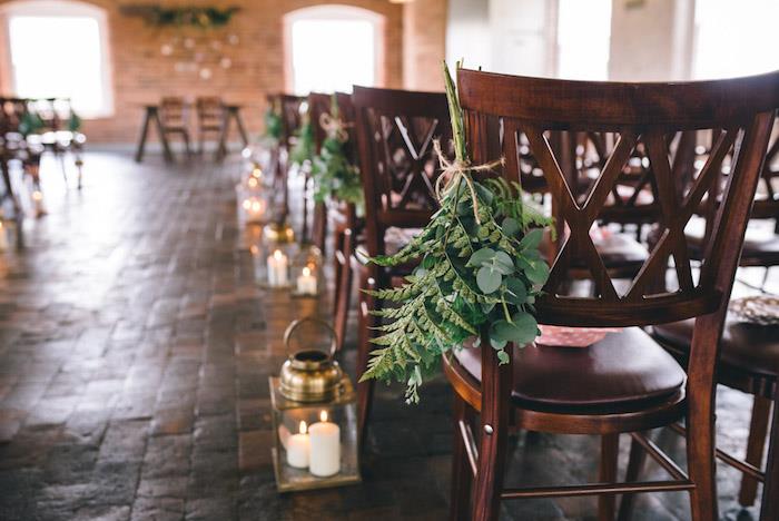 kaimiškas vestuvių dekoravimas vestuvių salei, akmeninė siena, žibintai su žvakėmis, gėlėtos medinės kėdės