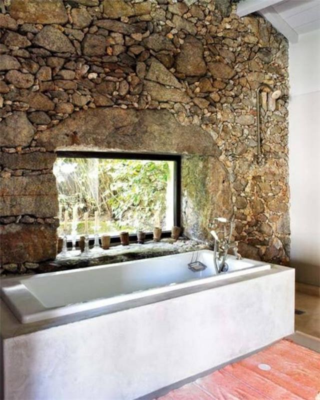 sienų apdaila su akmens efektu-siena ir balta vonia kaimiškame vonios kambaryje