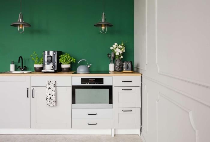 model majhne kuhinje, opremljene po dolžini s steno, pobarvano v temno zeleni barvi z belim pohištvom in lesenimi pulti
