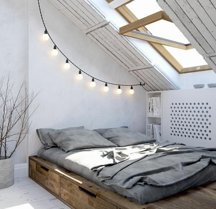 Skandinaviškas miegamojo palėpės apdaila-medinė lova su matomu čiužiniu-saugykla-elektros girlianda.