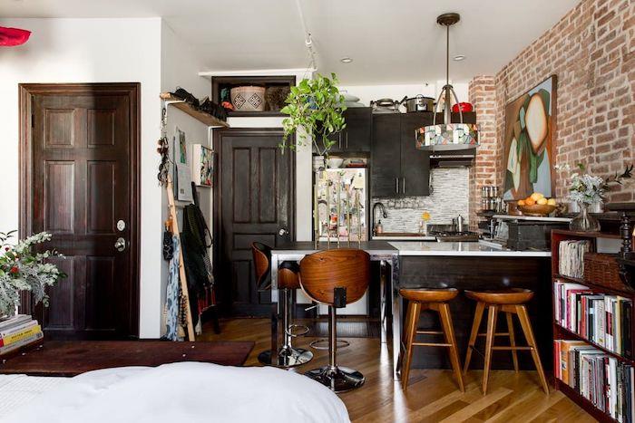 kaip įrengti nedidelę bistro stiliaus virtuvę mažame bute su rudais mediniais baldais, šviesaus medžio parketu, akcentine plytų siena, menine apdaila