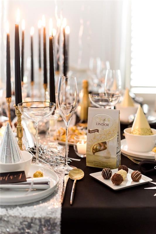 Silvestrska dekoracija mize dolge črne sveče, argentinski namizni tekač in škatla čokoladnih bonbonov
