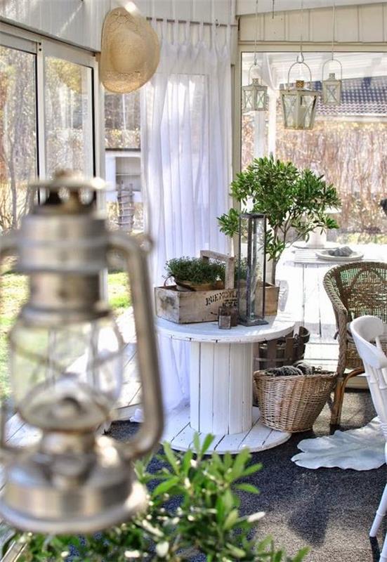 elegantna podeželska veranda deco, kolut za mizico, lesena košara, pohištvo iz ratana, siva preproga, okrasne luči
