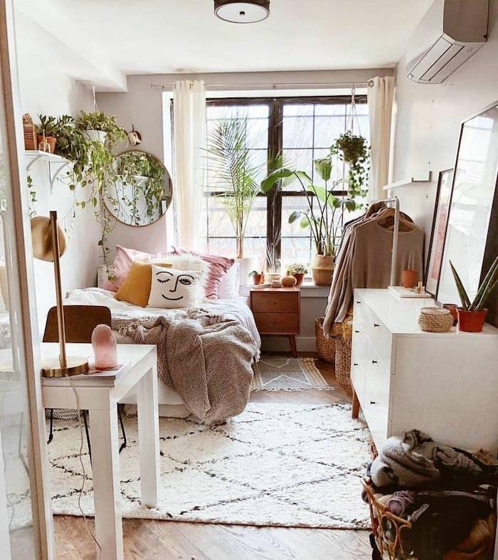 Skandinaviškai balta komoda, rožinė, geltona ir balta patalynė, pilka lovos užtiesalas, jaukus gauruotas kilimas, kambariniai žali augalai, džiunglių dekoras, šviesaus medžio parketas