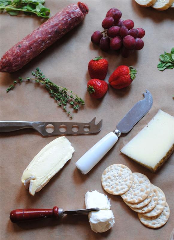 noži za sir in maslo jagode in grozdje na mizi z zelišči