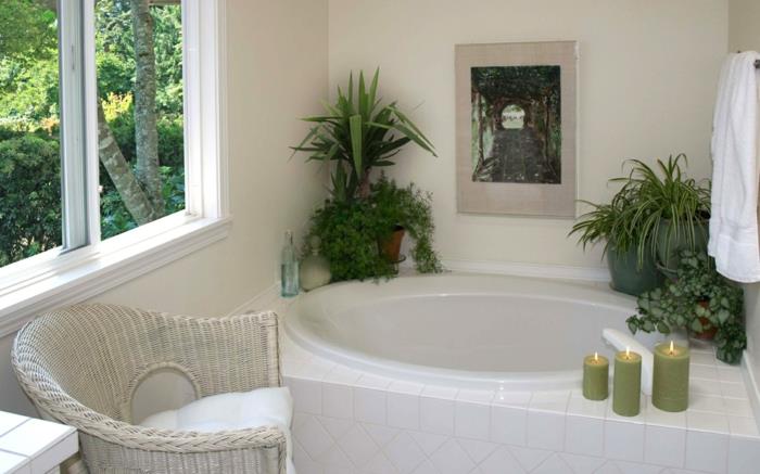 kambariniai augalai, mažas vonios kambarys, puodai, pastatyti ant mažos baltos ovalios vonios kraštų, trys didelės žalios žvakės, baltas rotango fotelis, vonia, padengta baltomis plytelėmis, didelis langas šalia vonios