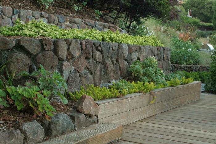 siena iš didelių rudų ir pilkų šiurkščių akmenų, išorinė augalinė siena žalia ir geltona, dalis šviesios medienos, kuri slepia žemę ir medžio žemę, veranda
