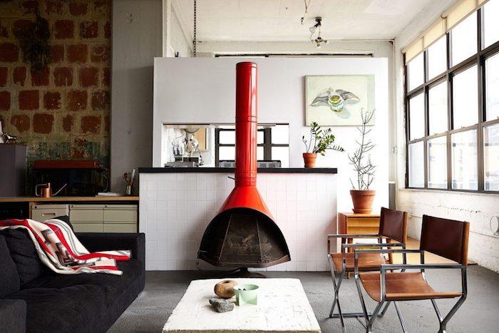 pohištvo v industrijskem slogu, usnjeni in kovinski stoli, siva talna obloga, črni kavč in rdeč kamin