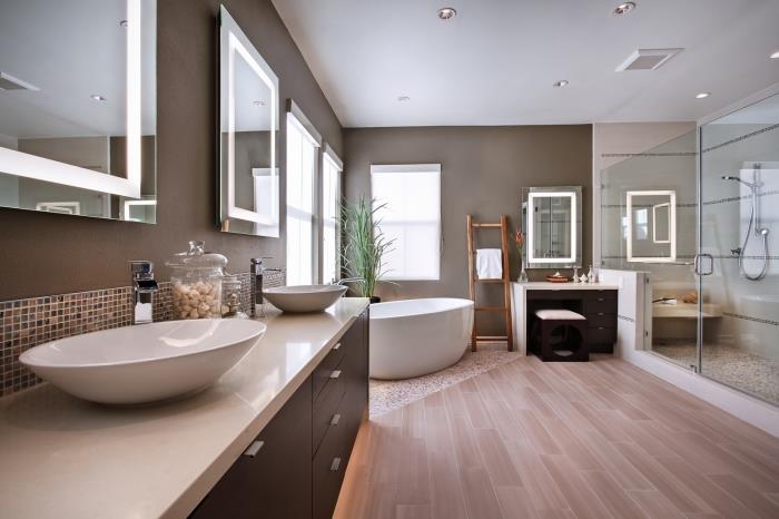 modernus medinis ir pilkas vonios kambarys, vonios kambario apdaila su pilkomis sienomis su šviesiomis medinėmis grindimis ir vonia ant mozaikinių plytelių