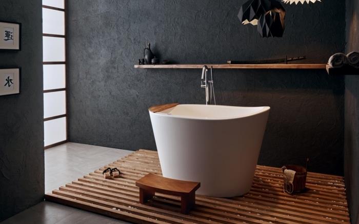 mažos baltos vonios modelis ant medinio kilimo, atsipalaiduokite azijietiško stiliaus vonios kambario apdaila su tamsiomis sienomis ir medžio akcentais