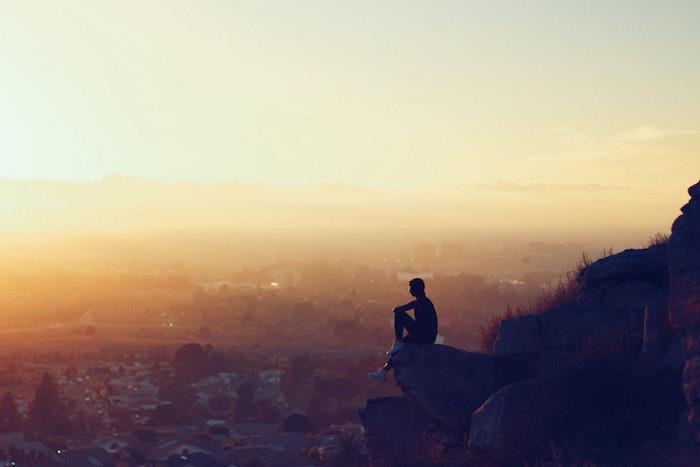 Človek, ki sedi na skali s čudovitim razgledom ob sončnem zahodu, čudovita mestna pokrajina, slika za ozadje brezplačna