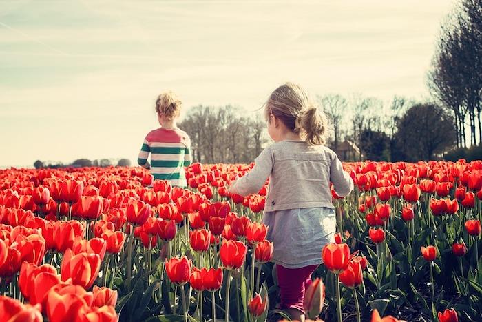 Dve dekleti, ki tečeta na cvetličnem polju, ozadje podeželske pokrajine, izvirna pokrajina ozadja tulipanov, ideja za ozadje