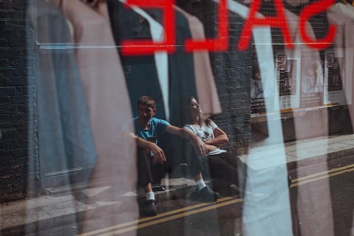 du žmonės priešais parduotuvės langą, kuriame siūlomos nuolaidos juodojo penktadienio sandoriui