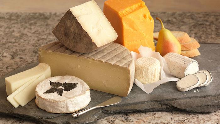 različne vrste sira na kamnitem krožniku z nožem za maslo