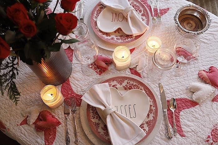 vakarienė žvakių šviesoje ant baltos staltiesės, papuoštos mažomis audinio širdelėmis vazoje su raudonomis rožėmis