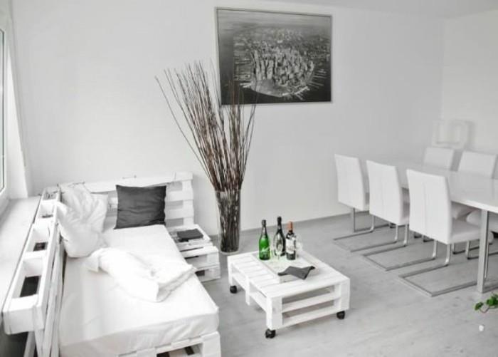 minimalistinis baltos ir šviesiai pilkos spalvos interjeras, modernus valgomojo stalas su šešiomis kėdėmis, padėklų sofa ir derantis kavos staliukas, didelė pilkos spalvos nuotrauka ant sienos, dekoratyvios džiovintos šakos vazoje