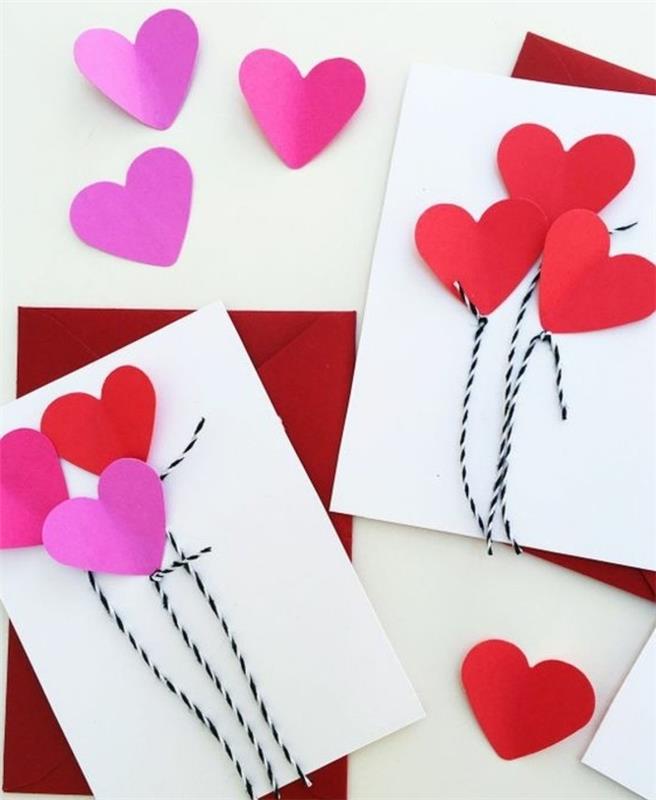 dve beli razglednici, okrašeni z rožnatimi in rdečimi oblikami srca ter črno -belo nitjo, položeni nad dve rdeči ovojnici, v bližini več rožnatih in rdečih oblik srca