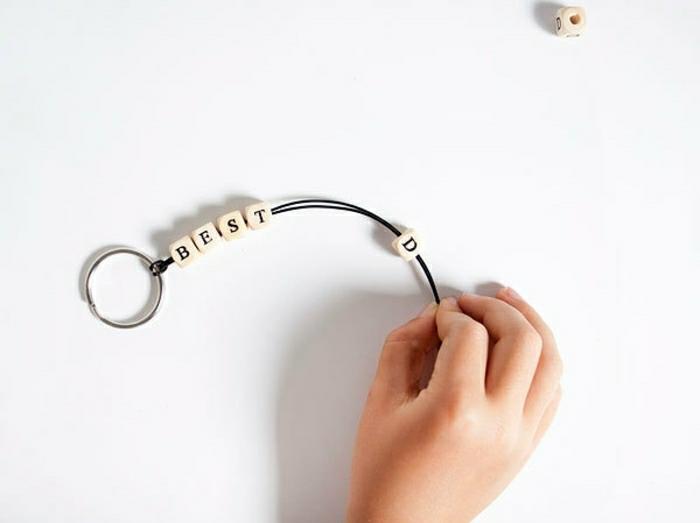 ideje za darila za dan očeta, otroška roka, ki drži kos usnjene vrvice z abecednimi kroglicami, ki se najbolje črkuje, vezana na obesek za ključe