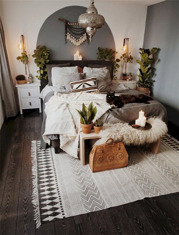 bohemiško miegamojo dekoro pavyzdys su etniniais daiktais, kambarys su baltomis sienomis su pilku sienų dekoru ir tamsiu parketu