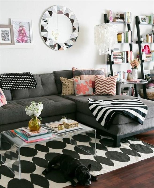 šviesiai pilkos sienos, pilka kampinė sofa, spalvota spauda, ​​pagalvės, medinės knygų lentynos, stiklinis kavos staliukas
