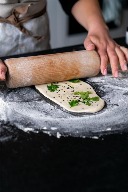 Açılan hamur, maydanoz ve sarımsak, üzerine çörek otu koyulur, naan ekmeği tarifi, unla kaplanmış siyah yüzey