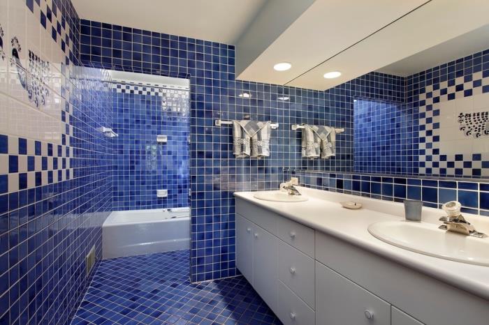 bele in temno modre ploščice v sodobni kopalnici z LED osvetlitvijo in belim pohištvom, belo kadjo in mornarsko modrimi ploščicami