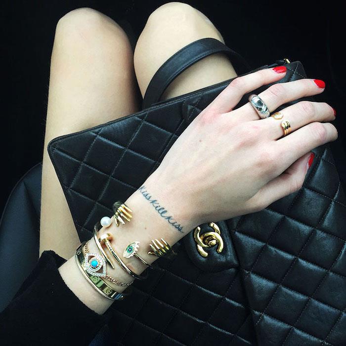 črna usnjena torbica, črni plašč za ženske, zlate zapestnice z biseri in kristali, majhna tetovaža na roki