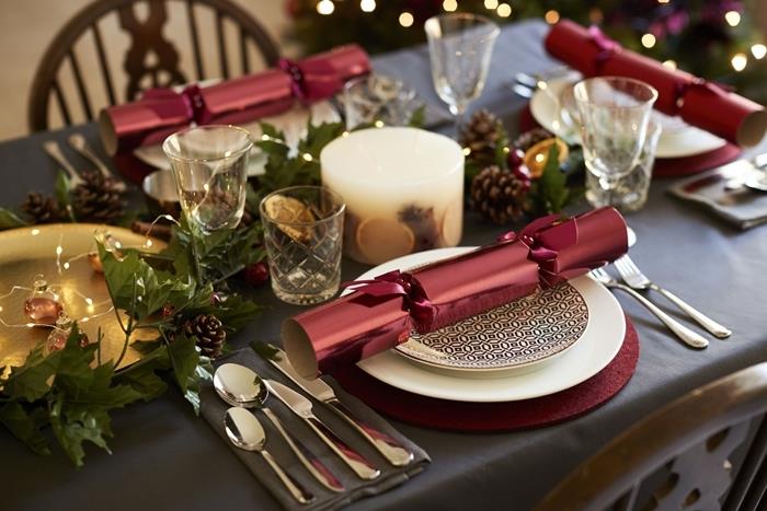 rdeča božična miza ovojno darilo bela okrogla plošča zlati pladenj steklene sveče suho sadje borov stožec
