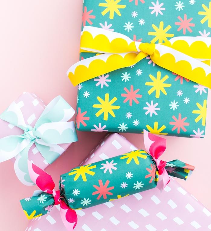 Božični darilni ovojni papir modre barve in pisani vzorci snežink, paket v obliki kocke in valja ter modri, roza in rumeni trak