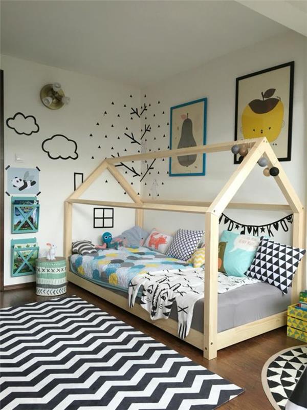 parmaklıksız bebek karyolası, montessori yatak odası, grafik desenli büyük siyah beyaz halı, beyaz duvarda siyah tasarımlar, bulutlar, ağaç ve pencere ve ev şöminesi