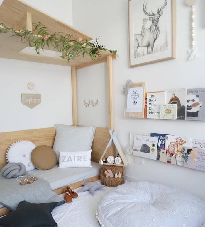 medinė lova ant grindų su mediniu stogu, vaikiškos pagalvėlės neutraliomis spalvomis, minimalistinės lentynos ant baltos sienos, baltas pufas