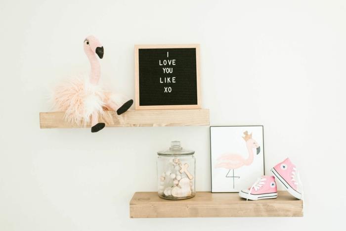 dodatek flamingo, police iz svetlega lesa na kremno beli steni v vrtcu, okrasna slika z ljubezenskim sporočilom, majhne roza superge, stekleni kozarec z okrasnim srčkom in križem