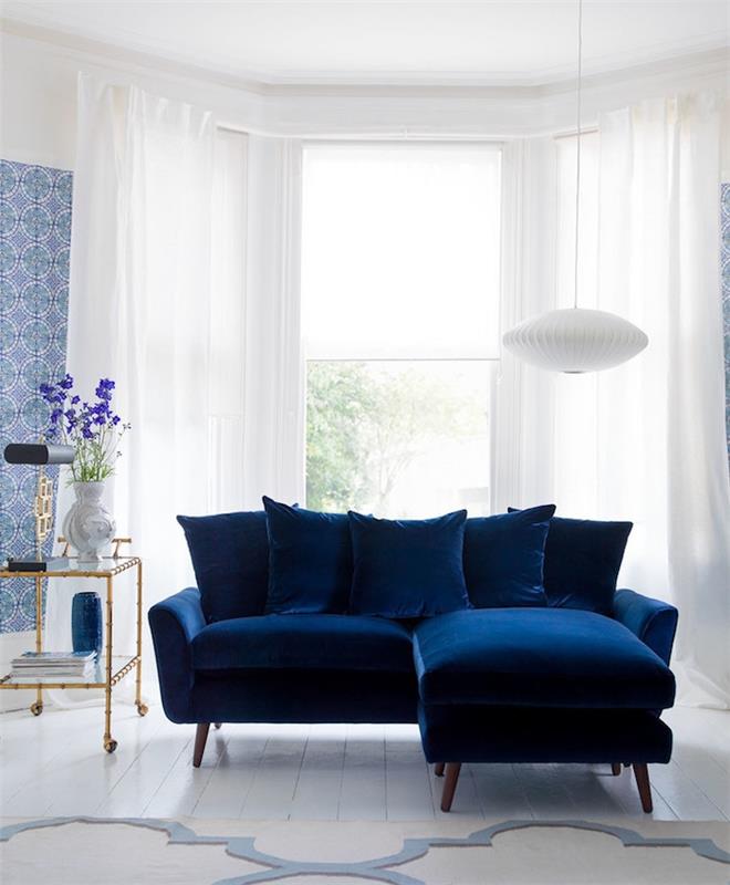 model polnočno modrega kavča v beli dnevni sobi z belim in modrim ozadjem s cvetličnim tiskom