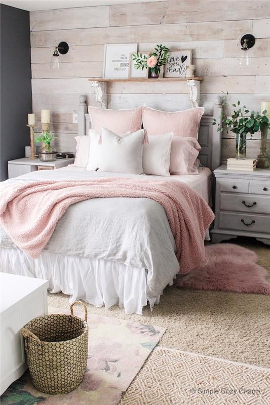 prašmatnus kaimiškas miegamojo dekoras, rožinės ir pilkos spalvos miegamojo idėjos, patinuota pilka naktinė spintelė, medinė siena, rožinės pagalvėlės ir lovos užtiesalas