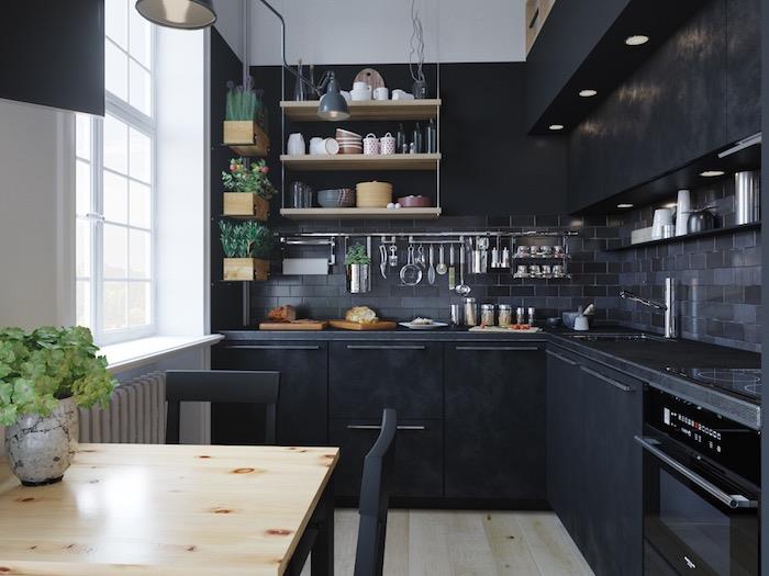 juodas l formos virtuvės modelis su antracito pilkos spalvos plytelėmis, medinė ir metalinė lentyna, dekoratyvinė gėlių dėžutė ir nedidelė valgomojo zona su mediniu stalviršiu ir juodomis kėdėmis