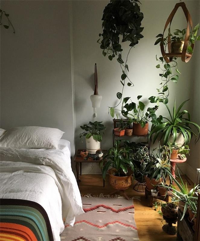 sive zelene stene v sobi v džungli z posteljo več rastlin, svetlim lesenim parketom, belim perilom in barvno odejo