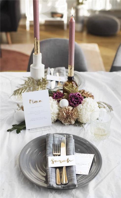 Primer novoletne dekoracije mize s sivim krožnikom in prtičkom, osrednji del s svečami in šopkom rož