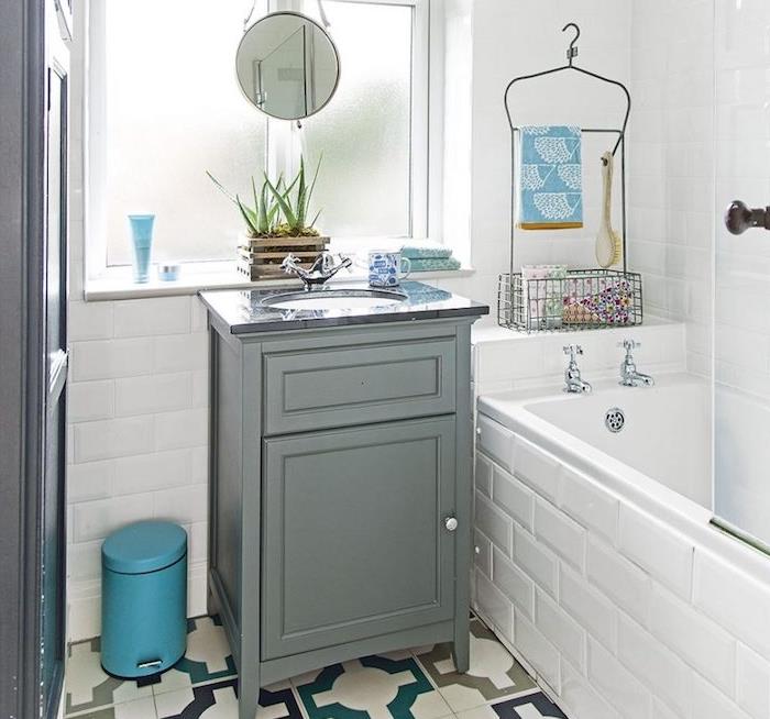 gömme küvet, gri dolap, beyaz duvar karoları ve retro desenli yer karoları, küçük yuvarlak ayna ile küçük bir banyo örneği