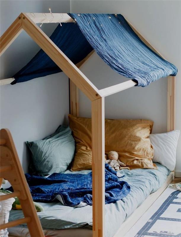vaikų kambariui pasirinkite montessori kajutę su pilkais čiužiniais, pagalvėmis ir pagalvėmis bei tamsiai mėlynos vilnos lovos baldakimu.